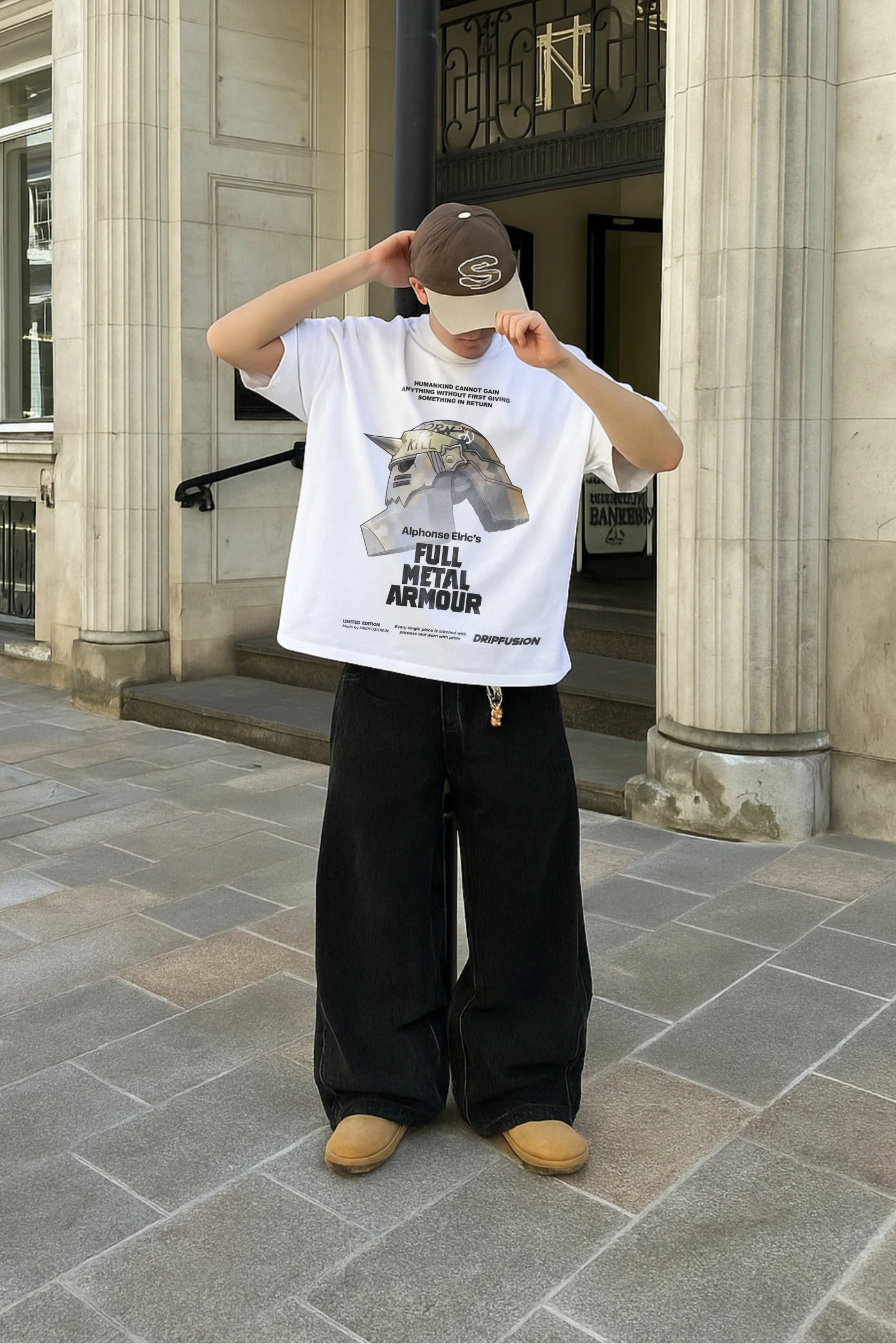 Person wearing a white t-shirt with full metal alchemist anime graphic design and text, standing in front of a building.